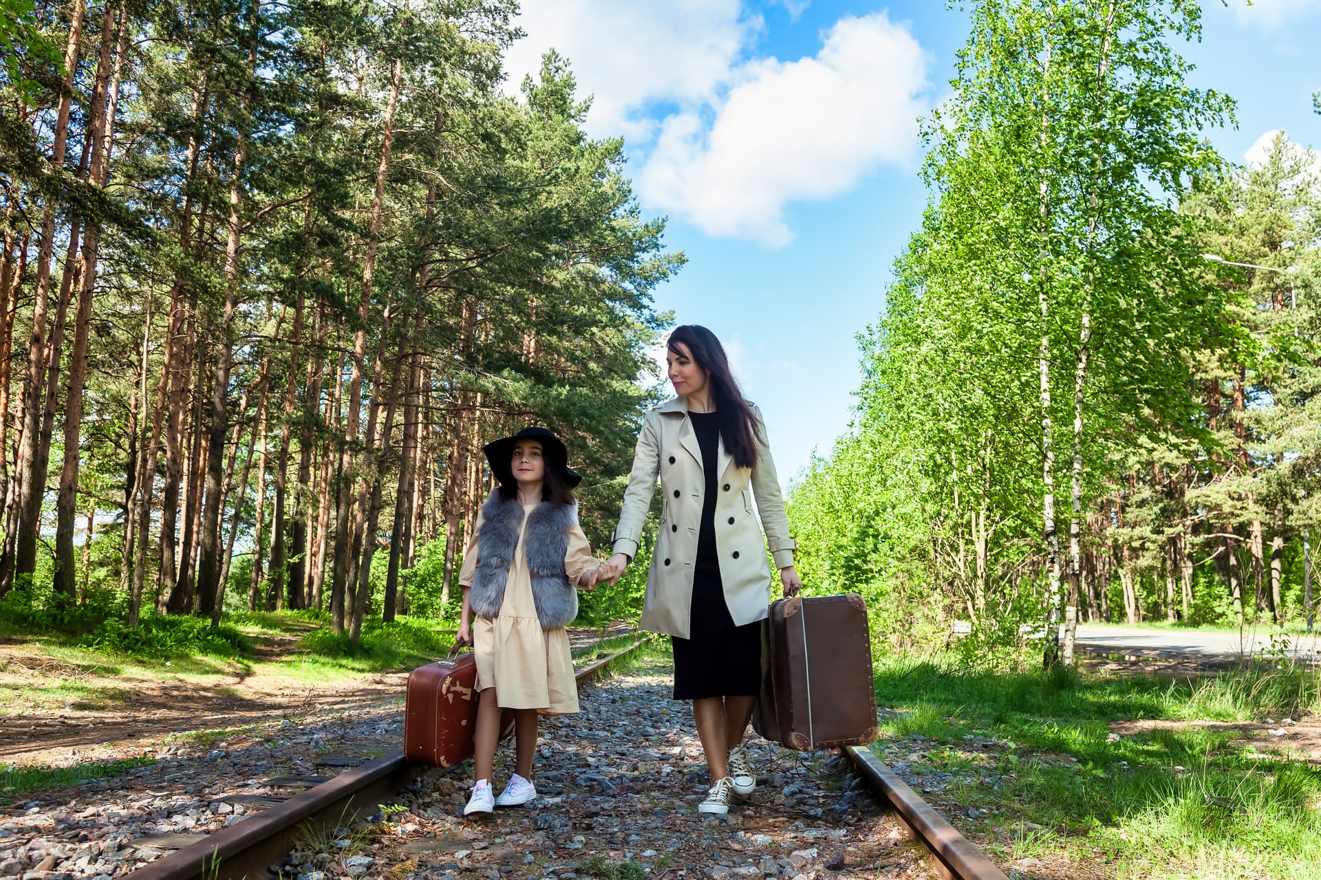 Mom and daughter, holding hands, with old suitcases (Algert Pateqi)